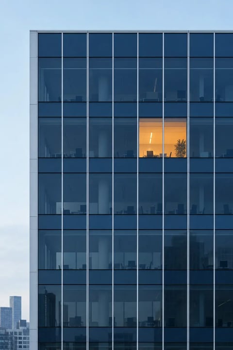 A navy glass office facade at night with a single window lit orange