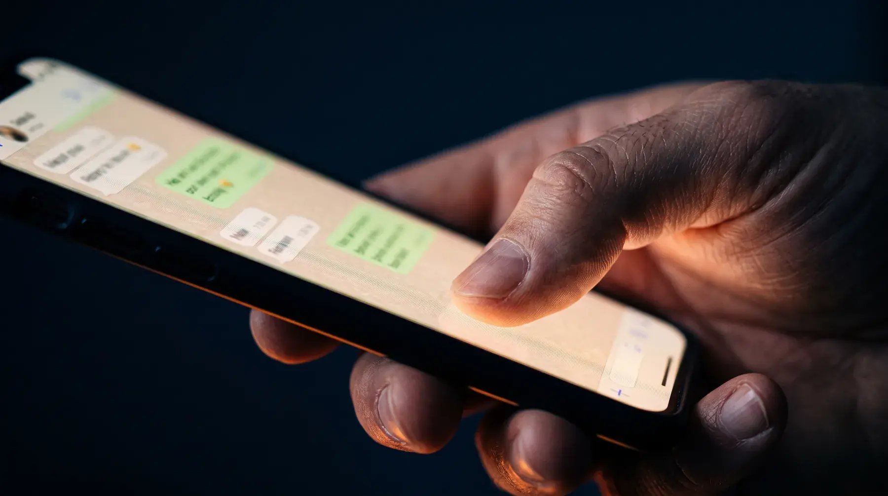 A hand holding a phone with a WhatsApp conversation glowing on screen